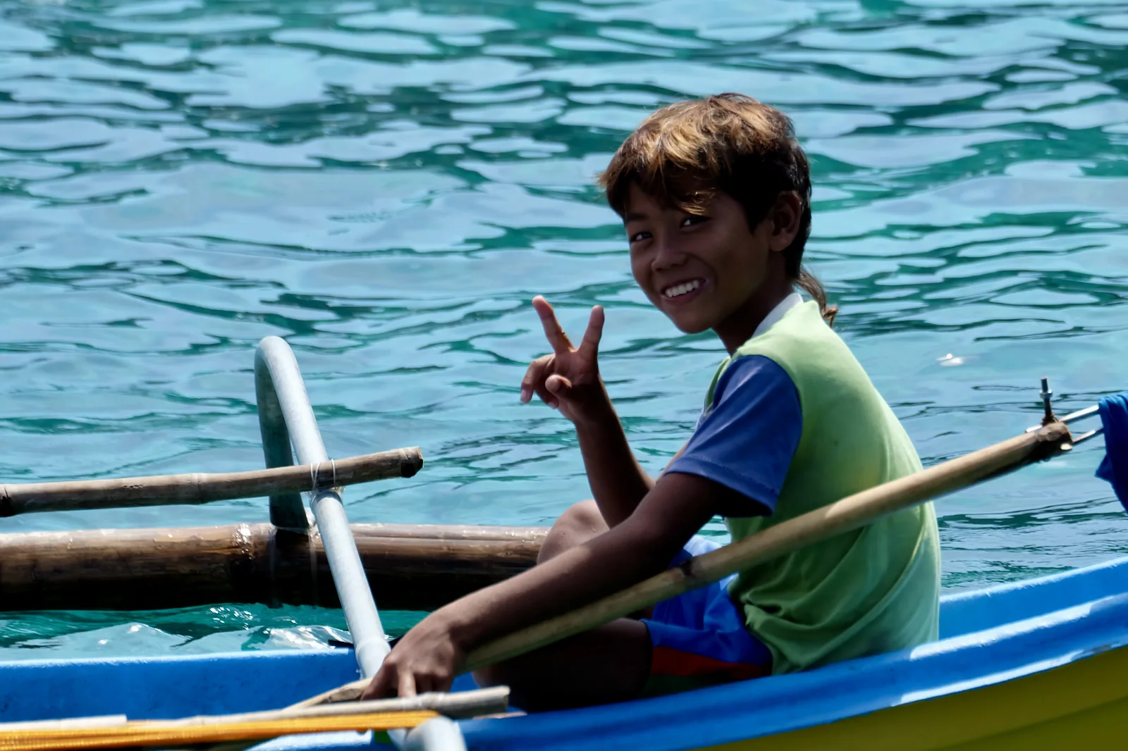 A smiling boy in a small blue and yellow boat on clear turquoise water.