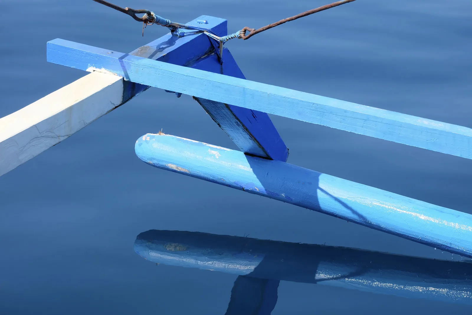 Close view of a blue-painted wooden outrigger resting on calm blue water.