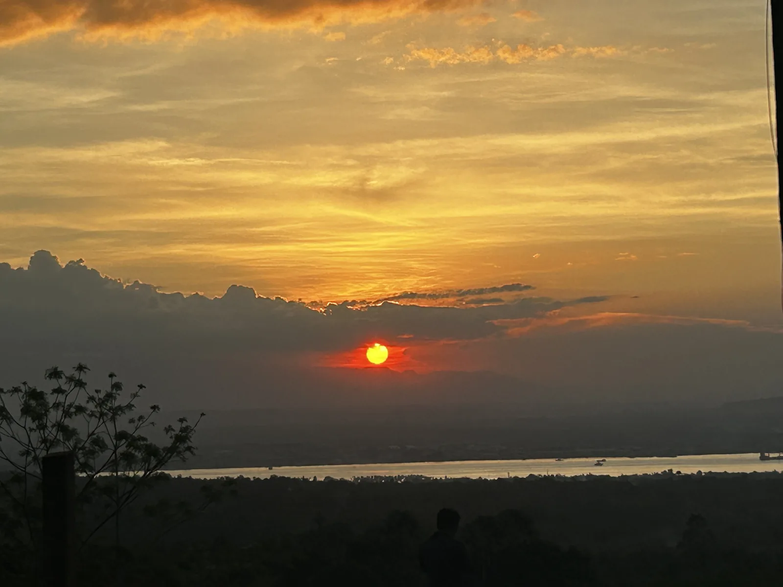 The sun setting behind a bank of cloud over the Davao Gulf, with boats on the water below.
